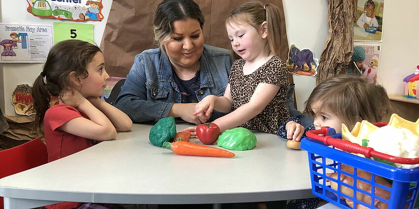 Photo of preschool students and teacher with plastic fruits and vegetables