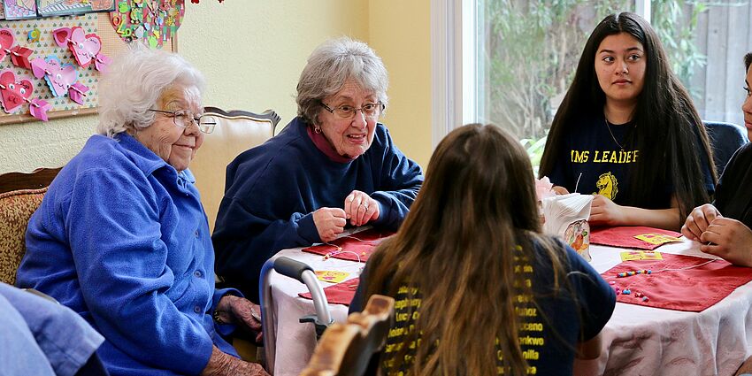 students work at table with elderly women