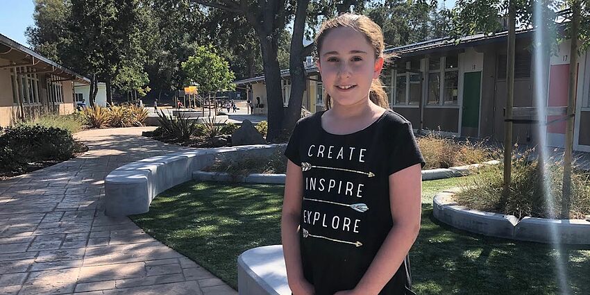 One girl standing, smiling at the camera and wearing a shirt that says Creating, Inspiring, Exploring.