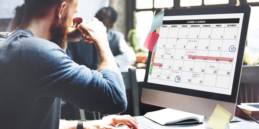 man drinking coffee while reading a calendar on his computer